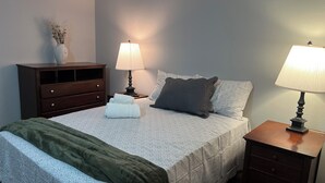 A neatly made bed with a patterned bedspread, two pillows, a green throw blanket, and a bedside table with a lamp. - Terrific 3-bedroom townhome with AC in charming Fargo, Central location (Fargo)
