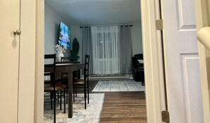 A dining area with a wooden table, chairs, a vase with white flowers, and a television on the wall.