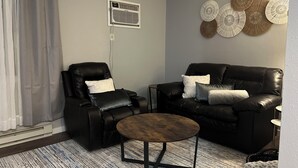 A living room with a black leather sofa, a black leather armchair, a round coffee table, a grey wall, and a decorative wall hanging. - Terrific 3-bedroom townhome with AC in charming Fargo, Central location (Fargo)