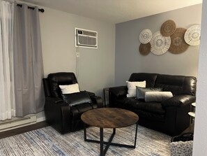 Ein Wohnzimmer mit einem schwarzen Ledersofa, einem schwarzen Ledersessel, einem runden Couchtisch, einer grauen Wand und einer dekorativen Wandleiste.