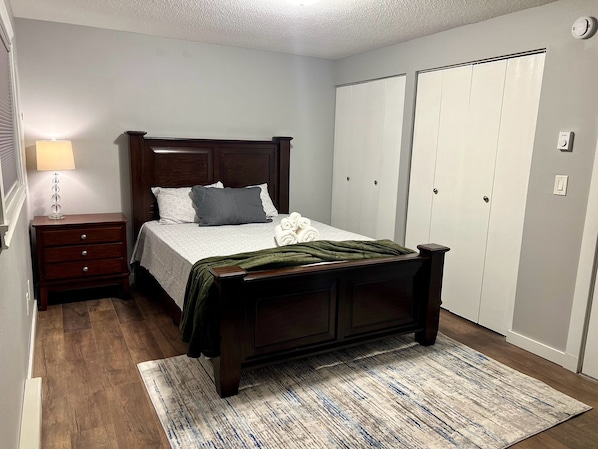 A bedroom with a wooden bed, a nightstand, a lamp, a green throw blanket, and a closet with sliding doors. - Terrific 3-bedroom townhome with AC in charming Fargo, Central location (Fargo)