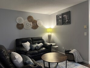 A modern living room with a black leather sofa, a round coffee table, and decorative wall art. - Terrific 3-bedroom townhome with AC in charming Fargo, Central location (Fargo)