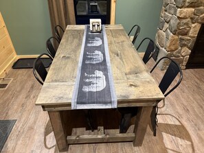 A wooden dining table with a black and white design, surrounded by black chairs, in a room with a stone wall and a door in the background.