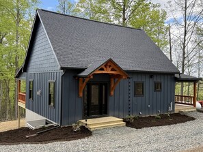 A modern building with a dark exterior, a wooden porch, and a gravel driveway.