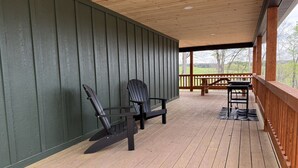 Un portico in legno con ringhiera, due poltrone Adirondack e un tavolo.