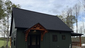 Un edificio verde con tetto scuro, un portico in legno e un vialetto sterrato.