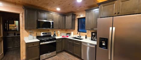 A modern kitchen with stainless steel appliances, wooden cabinets, and a wooden ceiling.