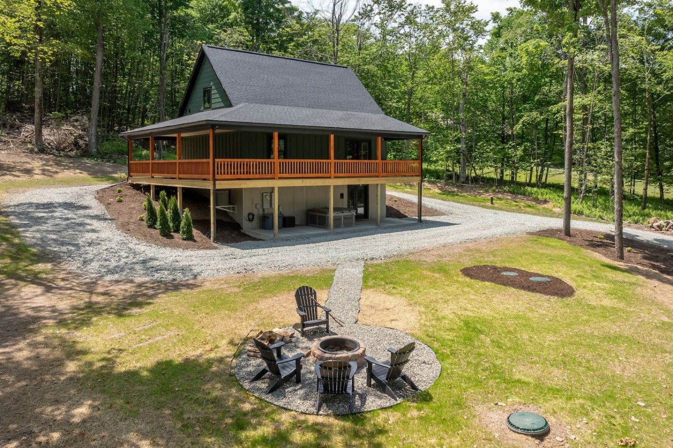 A cabin with a covered porch, a fire pit with chairs, and a gravel driveway.