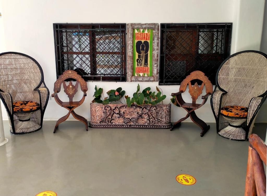 A room with two wicker chairs, a decorative wooden bench, and a window with decorative shutters.