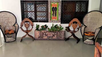 A room with two wicker chairs, a decorative wooden bench, and a window with decorative shutters.