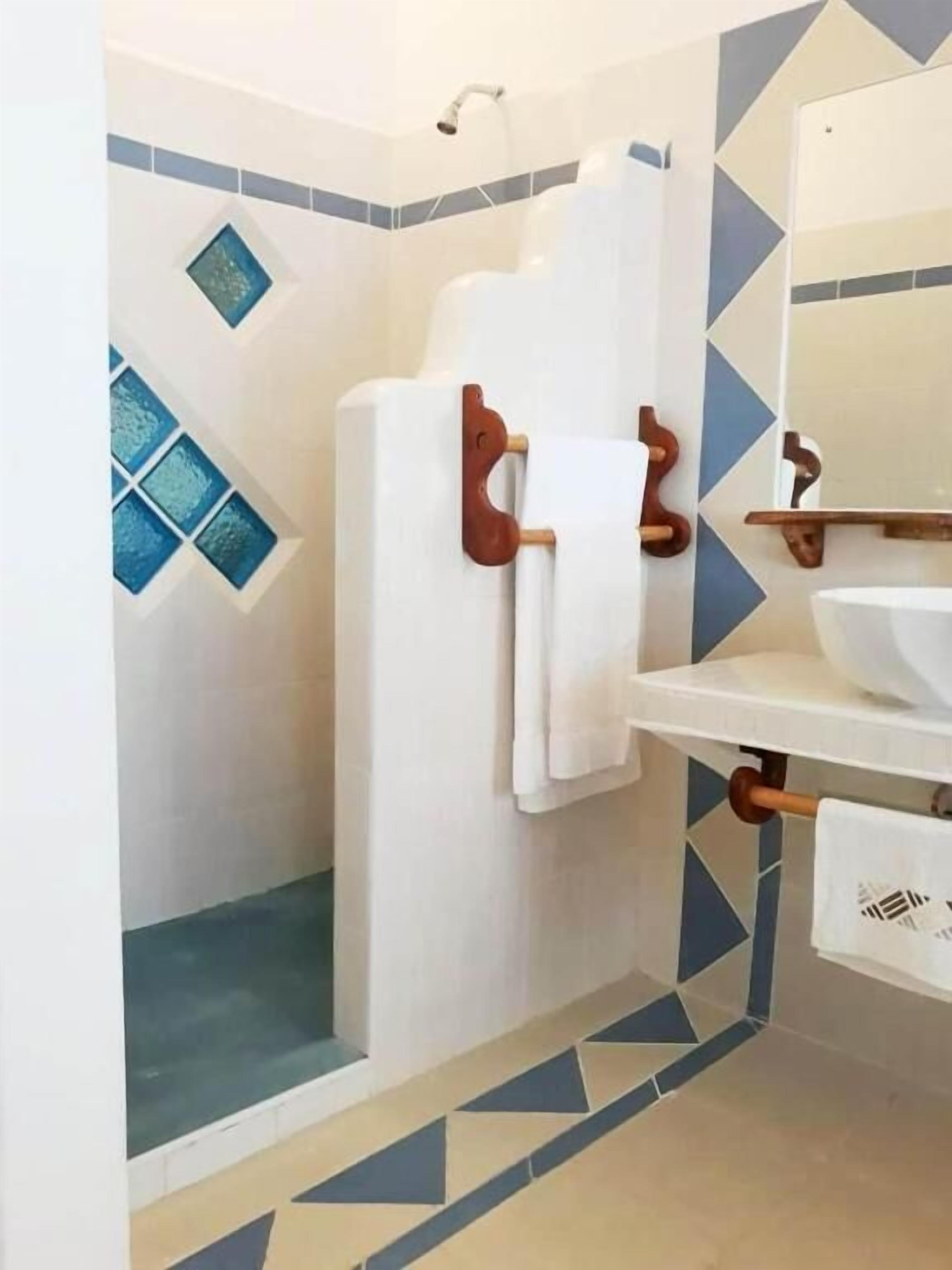 Une salle de bain avec un lavabo blanc, un miroir et une douche équipée d’un porte-serviettes en bois.