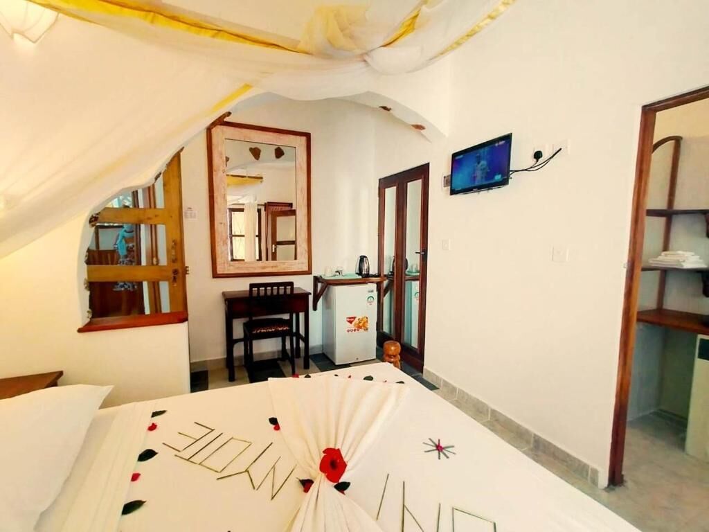 A bedroom with a bed, a desk, a chair, a television, and a mirror.