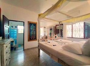 A bedroom with a canopy bed, a dresser, a mirror, and a window with decorative iron bars. - Solana Studio Apartments watamu (Watamu)