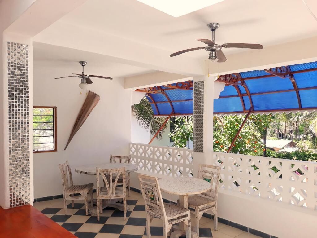 A room with a checkered floor, a white table with chairs, ceiling fans, and a view of greenery through a window.