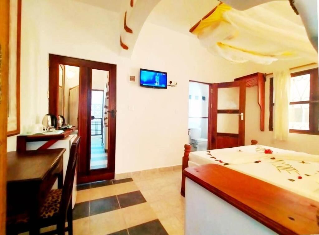 A hotel room with a bed, a desk with a chair, a television, and a door leading to another room.