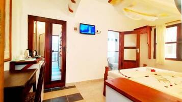 A hotel room with a bed, a desk with a chair, a television, and a door leading to another room.