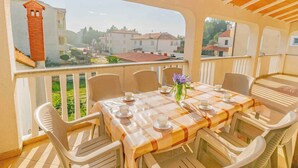 A balcony with a table set for four, chairs, and a view of buildings and greenery. - Holiday apartment with air conditioning and terrace (Medulin)