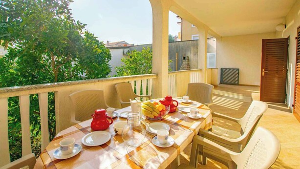 A balcony with a table set for breakfast, including plates, cups, and a fruit bowl. - Holiday apartment mit Klimaanlage (Medulin)