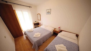 Un dormitorio con dos camas, suelo de madera, una mesita de noche con lámpara y una ventana con cortinas.