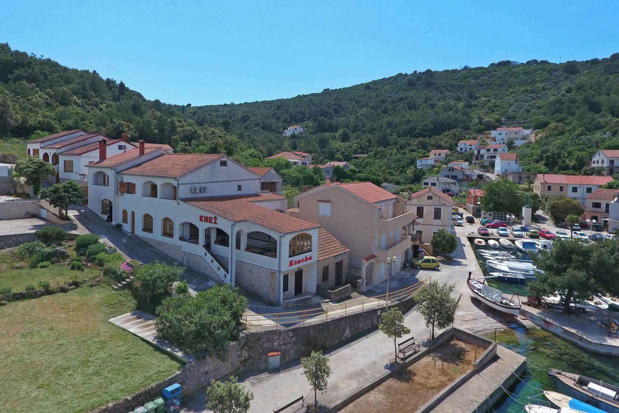 Un village côtier doté d’une architecture traditionnelle, un port de plaisance avec des bateaux et une colline en arrière-plan.