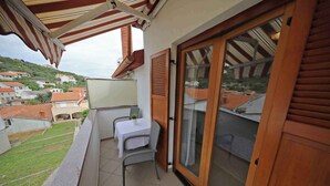 Un balcón con mesa y silla, un ventanal corredera y vista a una zona residencial.