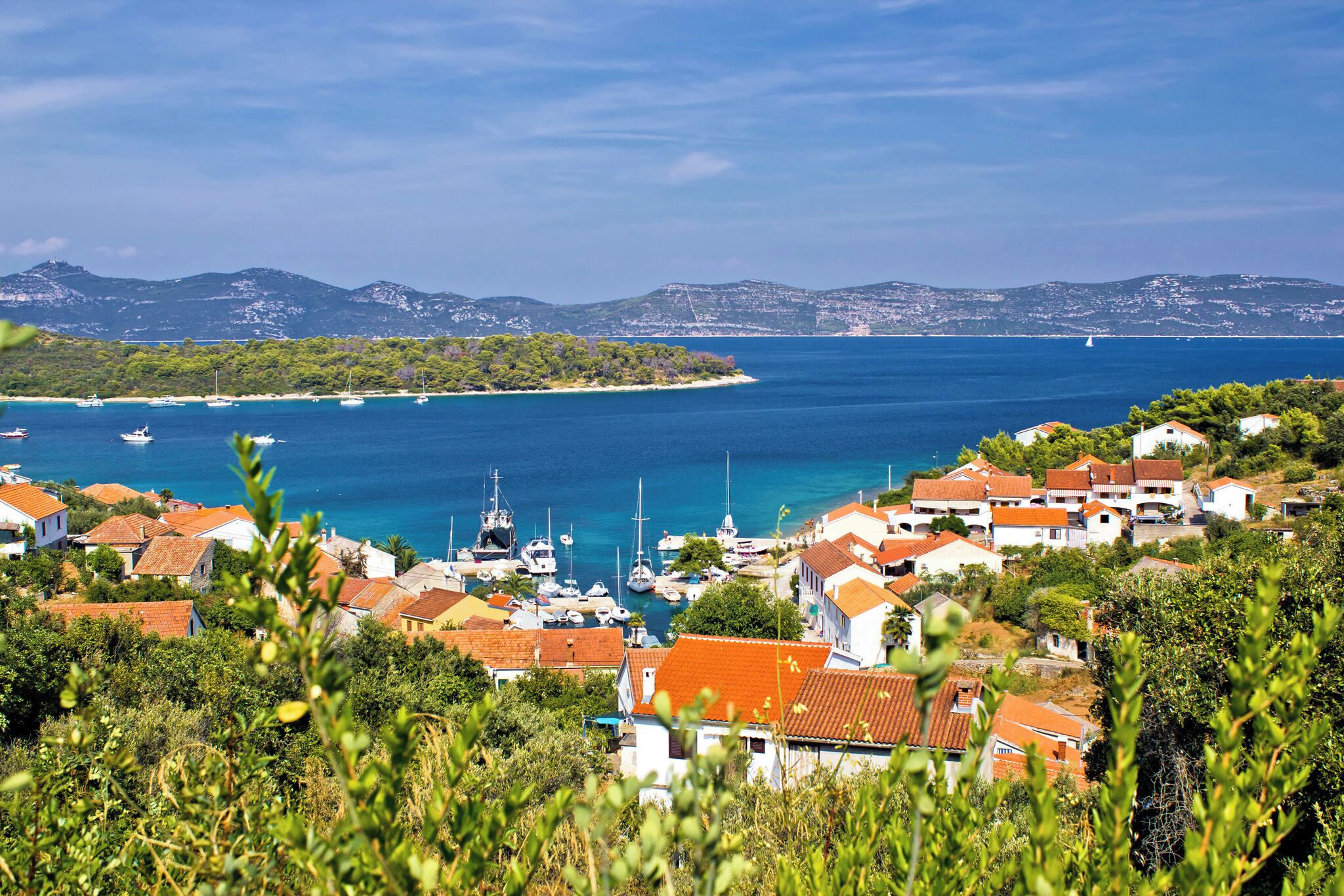 A coastal village with houses, boats, and a clear view of the sea and mountains.