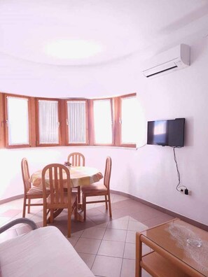 A room with a dining table, chairs, a TV mounted on the wall, and a bed. - Holiday apartment with air conditioning (Pula)