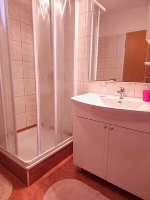 A bathroom with a glass shower enclosure, a white sink, and a mirror above it. - Holiday apartment with air conditioning (Pula)