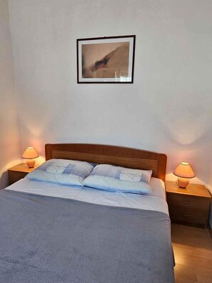 A neatly made bed with a blue blanket and pillows, flanked by two bedside tables with lamps. - Holiday apartment with air conditioning (Pula)