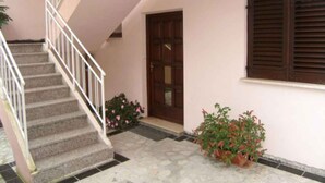 Una escalera que lleva a una puerta, una ventana con contraventanas y plantas en macetas.