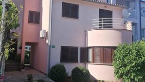 Un edificio residencial de varios pisos con fachada rosa, múltiples ventanas con contraventanas y un pequeño balcón.