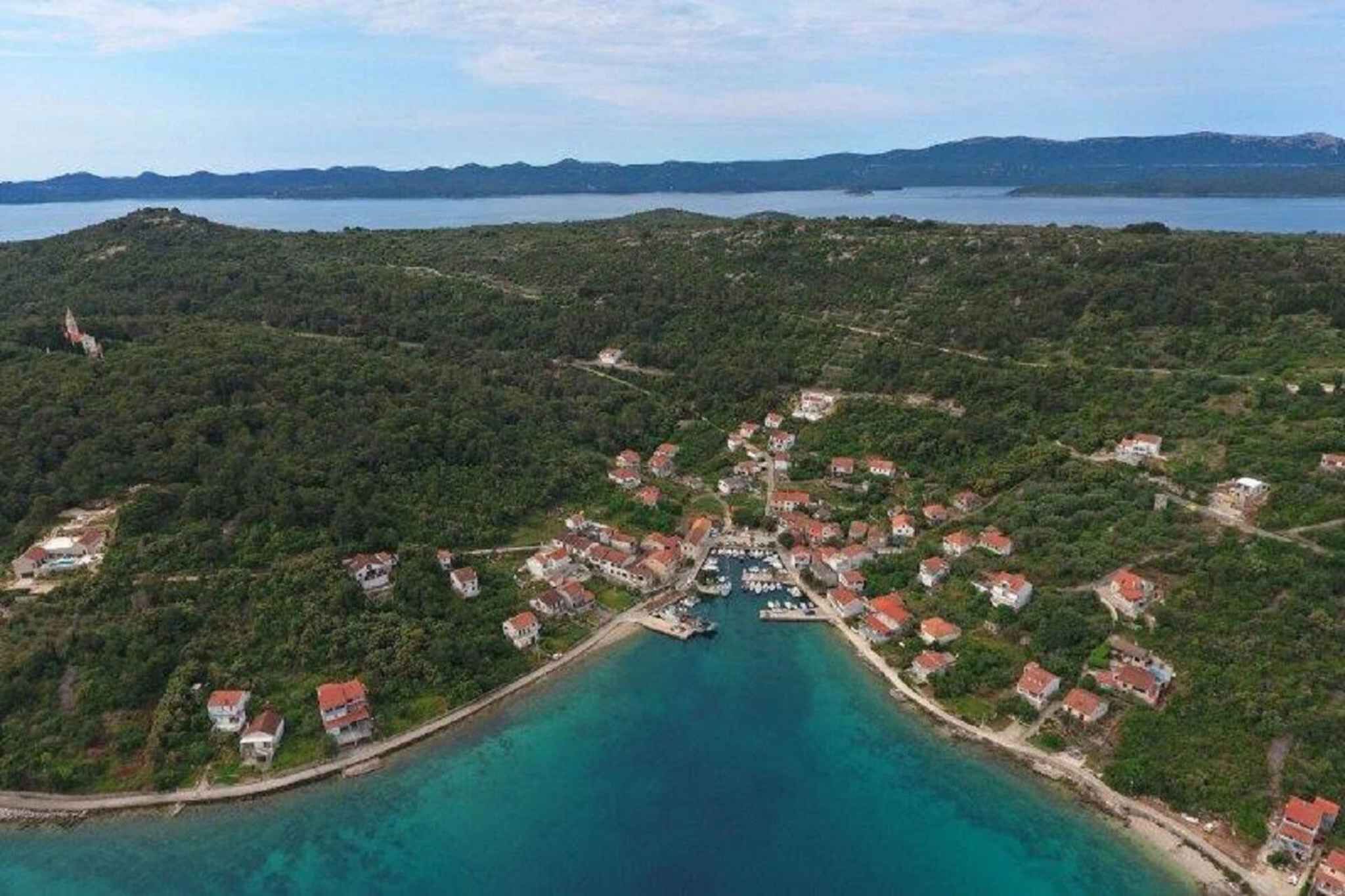 An aerial view of a coastal village with houses, a marina, and clear turquoise waters.