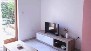 Ein modernes Wohnzimmer mit einem Flachbildfernseher auf einer Holzkonsole, einem kleinen Tisch und einer Schiebetür zu einem Außenbereich.