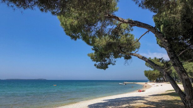 Una spiaggia con acqua cristallina, una riva sabbiosa e alcune persone che si rilassano.