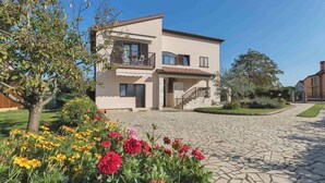 Una casa a due piani con un balcone, una scala in pietra e un giardino fiorito.