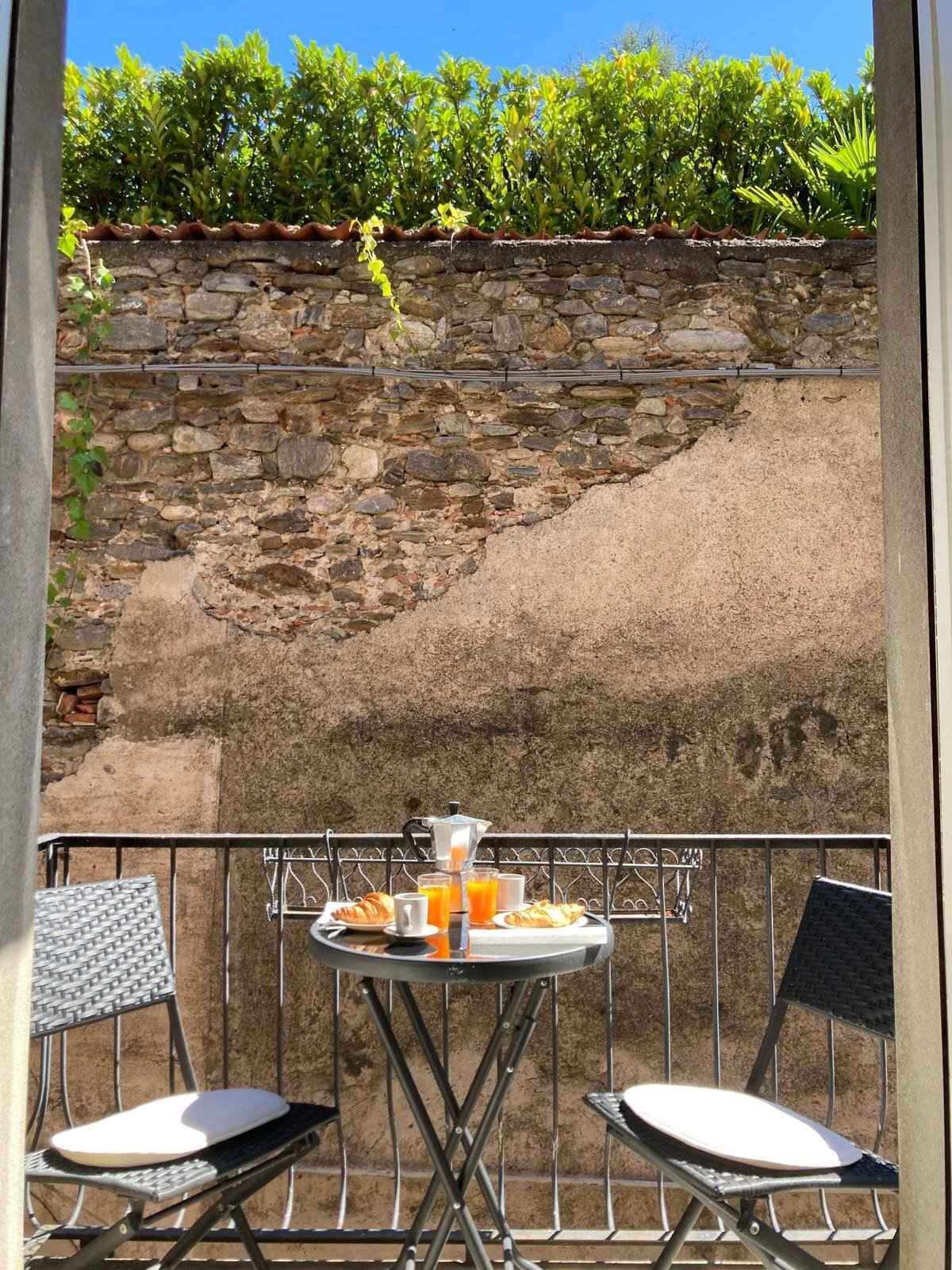 A balcony with a stone wall, a table with breakfast items, and two chairs.
