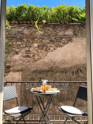 A balcony with a stone wall, a table with breakfast items, and two chairs. - Holiday apartment with balcony and internet (Lesa)