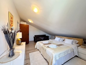 A bedroom with a sloped ceiling, two beds, a bedside table, a lamp, a chair, and a vase with branches. - Holiday apartment with balcony and sea view (Šilo)