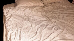 Una cama con sábanas blancas en una habitación con techo inclinado y cabecera oscura.