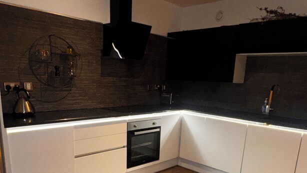Una cocina moderna con encimeras oscuras, armarios blancos y suelo de madera.