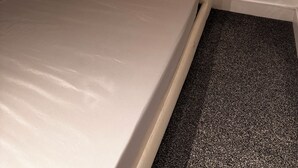 Una habitación pequeña con una cama individual, cabecera sencilla de color claro y suelo alfombrado.