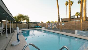 A swimming pool with a basketball hoop, lounge chairs, palm trees, and a covered seating area.