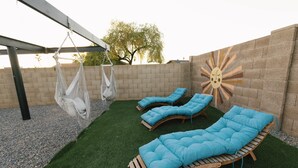 A patio with three wooden loungers, a hanging chair, and a sun mural on the wall. - Private Pool Oasis • 10 Min to Westgate & State Farm Stadium (Phoenix)