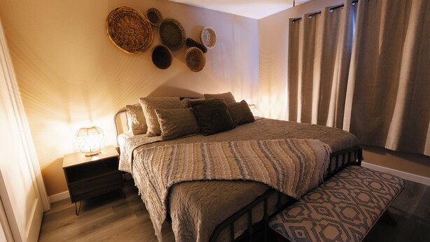 A bedroom with a bed, bedside tables, a bench, a wall with woven baskets, and a window with curtains. - Private Pool Oasis • 10 Min to Westgate & State Farm Stadium (Phoenix)