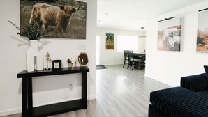 A modern living room with a black console table, a large painting of a yak, and a dining area with a white table and chairs. - Private Pool Oasis • 10 Min to Westgate & State Farm Stadium (Phoenix)