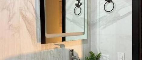A bathroom with a marble wall, a white sink, a mirror, and two wall-mounted towel rings.
