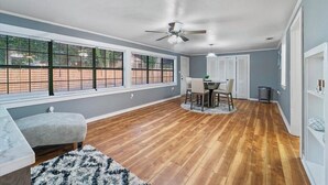 Una habitación amplia con zona de comedor, ventanas grandes y ventilador de techo.