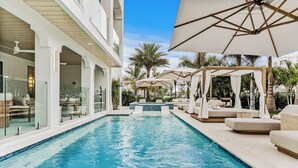 A pool area with a hot tub, lounge chairs, and umbrellas.