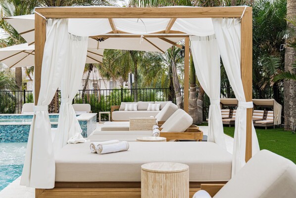 Un espace de détente extérieur luxueux, doté d’un lit à baldaquin, de linge de maison blanc et d’une piscine.