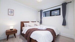 A neatly arranged bedroom with a bed, a bedside table with a lamp, a window with curtains, and a framed picture on the wall. - New Vancouver Kerrisdale Suite mins to Yvr/Ubc (Vancouver)